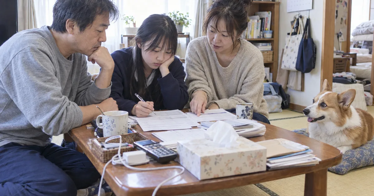 和室の座卓で資料を広げる10代の娘がいる家族と、座布団の上のウェルシュコーギー