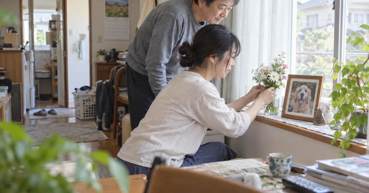 窓辺でゴールデンレトリバーの写真のそばに花を生ける女性